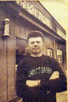 Vintage photo of a barber in a Carlo's Barbershop sweatshirt outside the shop